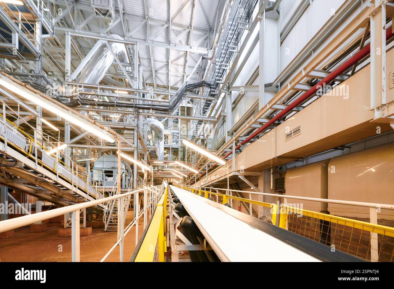À l'intérieur d'une usine chimique moderne présentant de vastes pipelines et un système de convoyeur en fonctionnement pendant les heures de jour Banque D'Images
