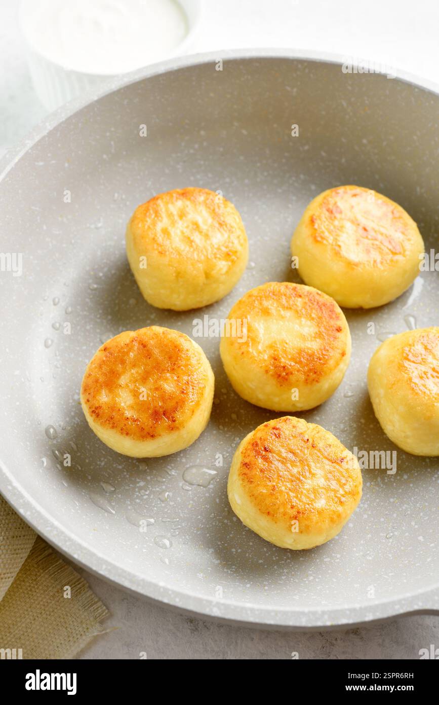 Vue rapprochée des crêpes au fromage cottage (beignets syrniki ou caillé) dans une poêle sur fond blanc. Banque D'Images
