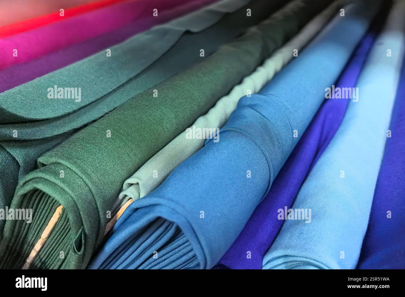 Les couleurs se mélangent harmonieusement tandis que les rouleaux de tissu sont soigneusement disposés, mettant en valeur un spectre de bleus et de verts. Les tailleurs et les designers peuvent trouver l'inspiration Banque D'Images
