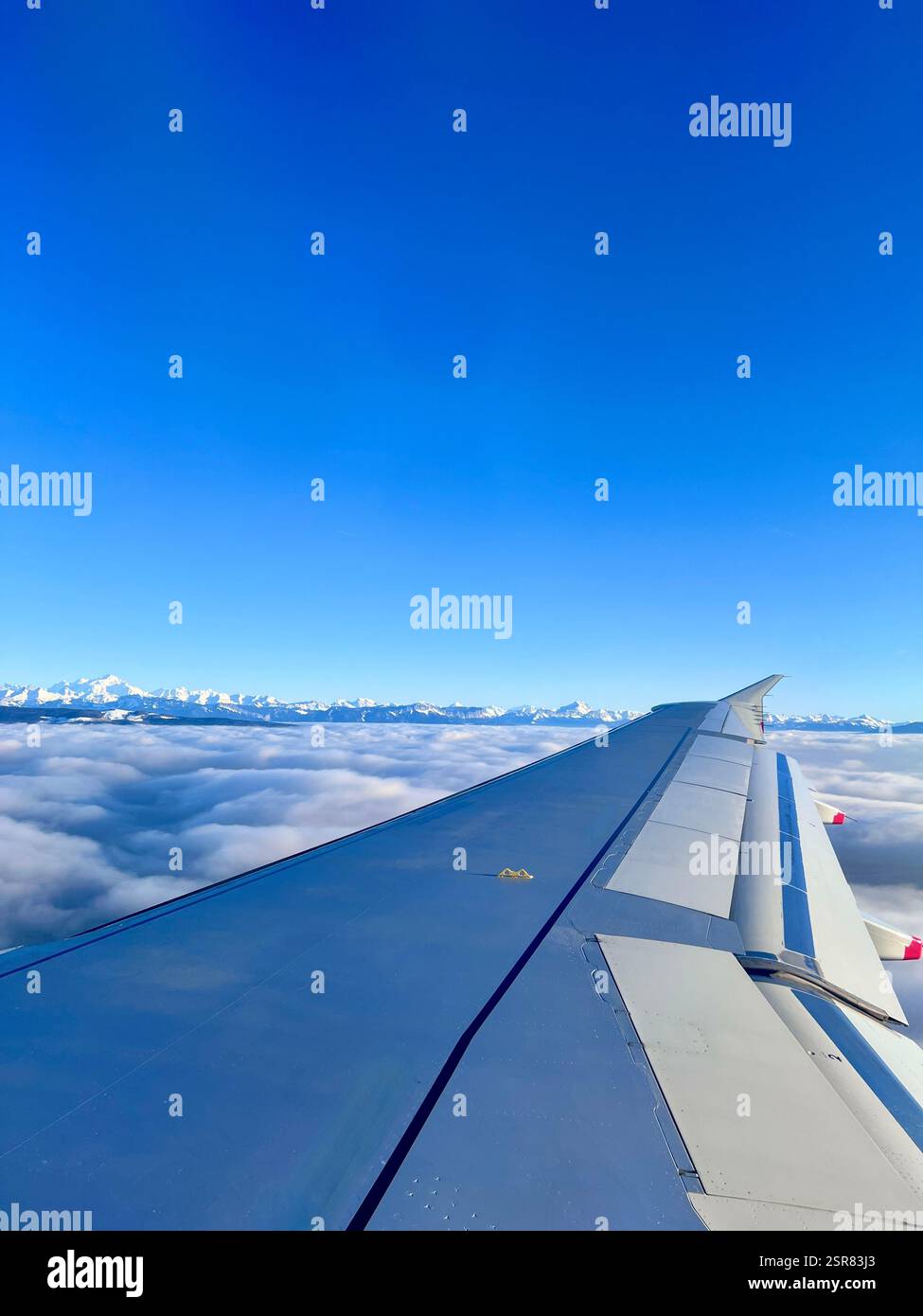 Vue depuis la fenêtre de l'avion d'un avion en vol avec aile. Vue au-dessus des nuages avec les alpes suisses au loin. Bleu vif, clair, ciel ensoleillé. Banque D'Images
