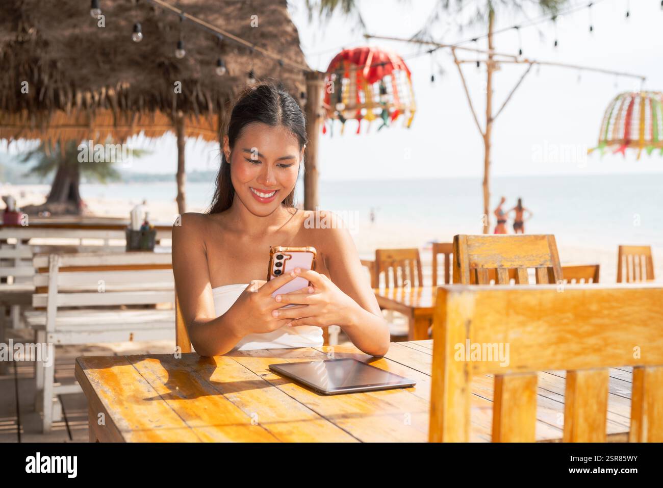 Jeune femme utilisant le téléphone portable sur la plage en Thaïlande Banque D'Images