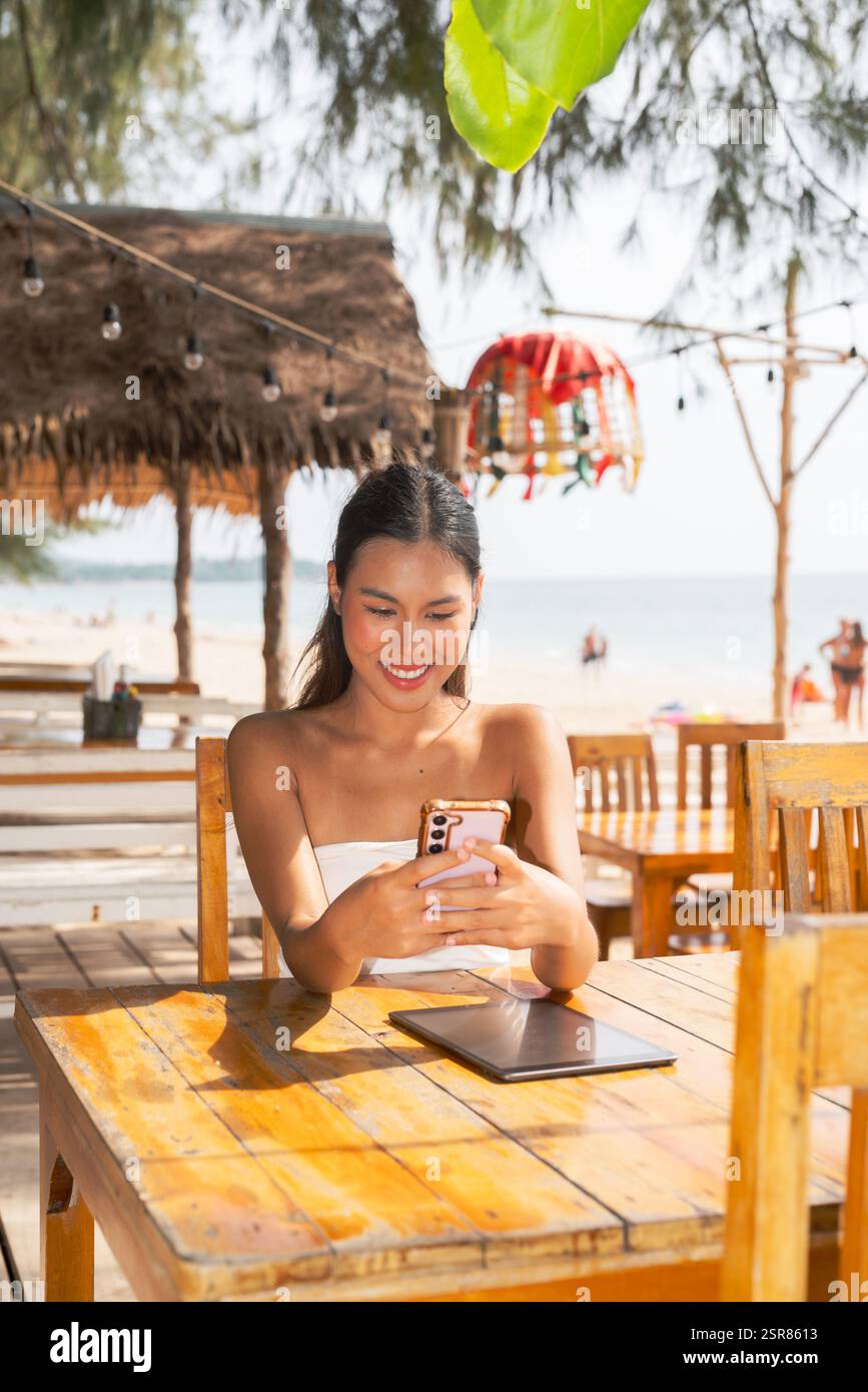 Jeune femme utilisant le téléphone portable sur la plage en Thaïlande Banque D'Images