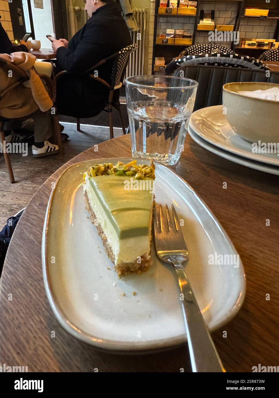 Une tranche de cheesecake crémeux est servie dans une assiette dans un café chaleureux, partiellement mangée. La scène capture l'indulgence et une atmosphère de café accueillante - Image de stock capturée avec un smartphone