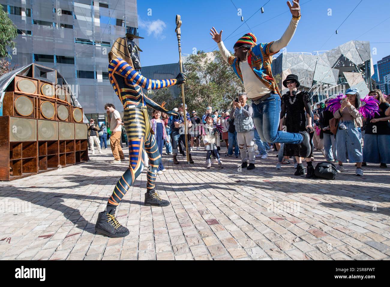 MELBOURNE, AUSTRALIE. 15 février 2025. Sur la photo : un homme aux couleurs rastafariennes saute dans les airs devant un artiste vêtu d'un costume du Dieu égyptien Anubis tenant une équipe au Festival Afro Caribbean, Federation Square, Melbourne, Australie le 15 février 2025. Crédit : Karl Phillipson / Alamy Live News Banque D'Images