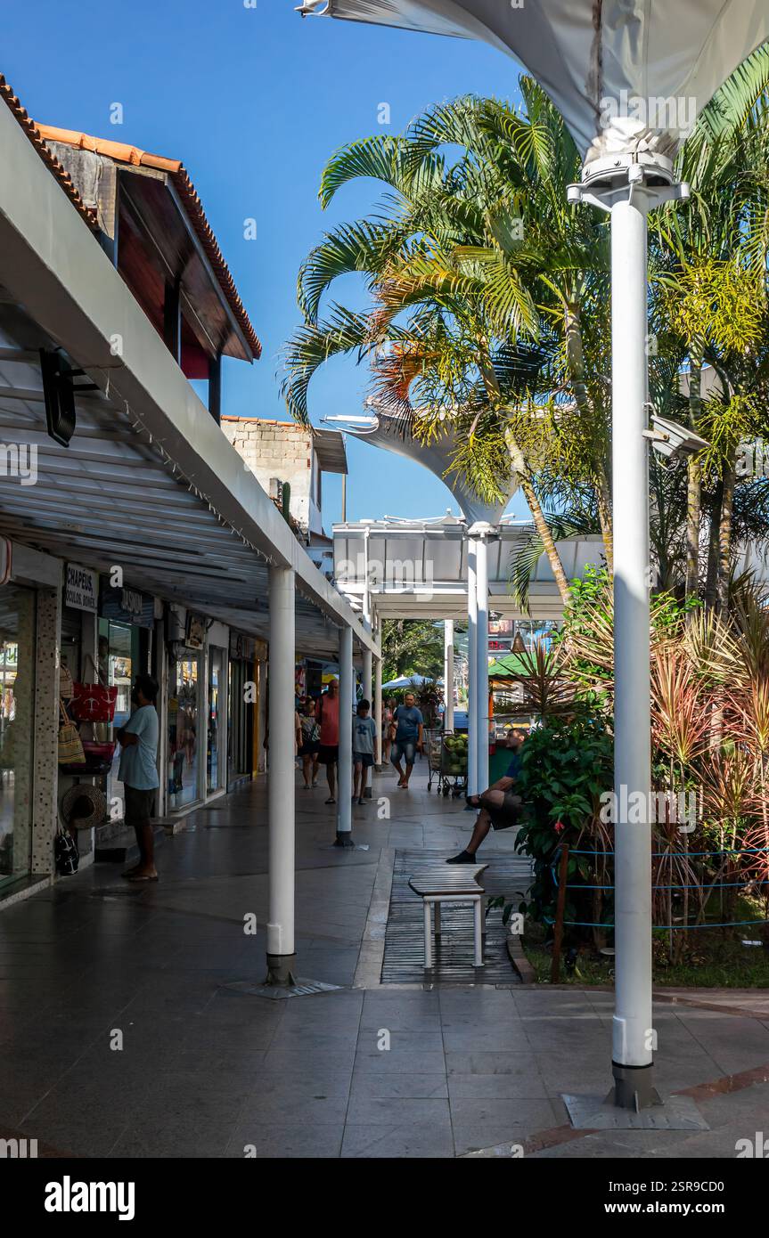 Couloir commercial ombragé du centre commercial Rua dos Biquínis dans le quartier Gamboa avec des magasins, un aménagement paysager vert et des gens se promenant sous un après-midi d'été. Banque D'Images