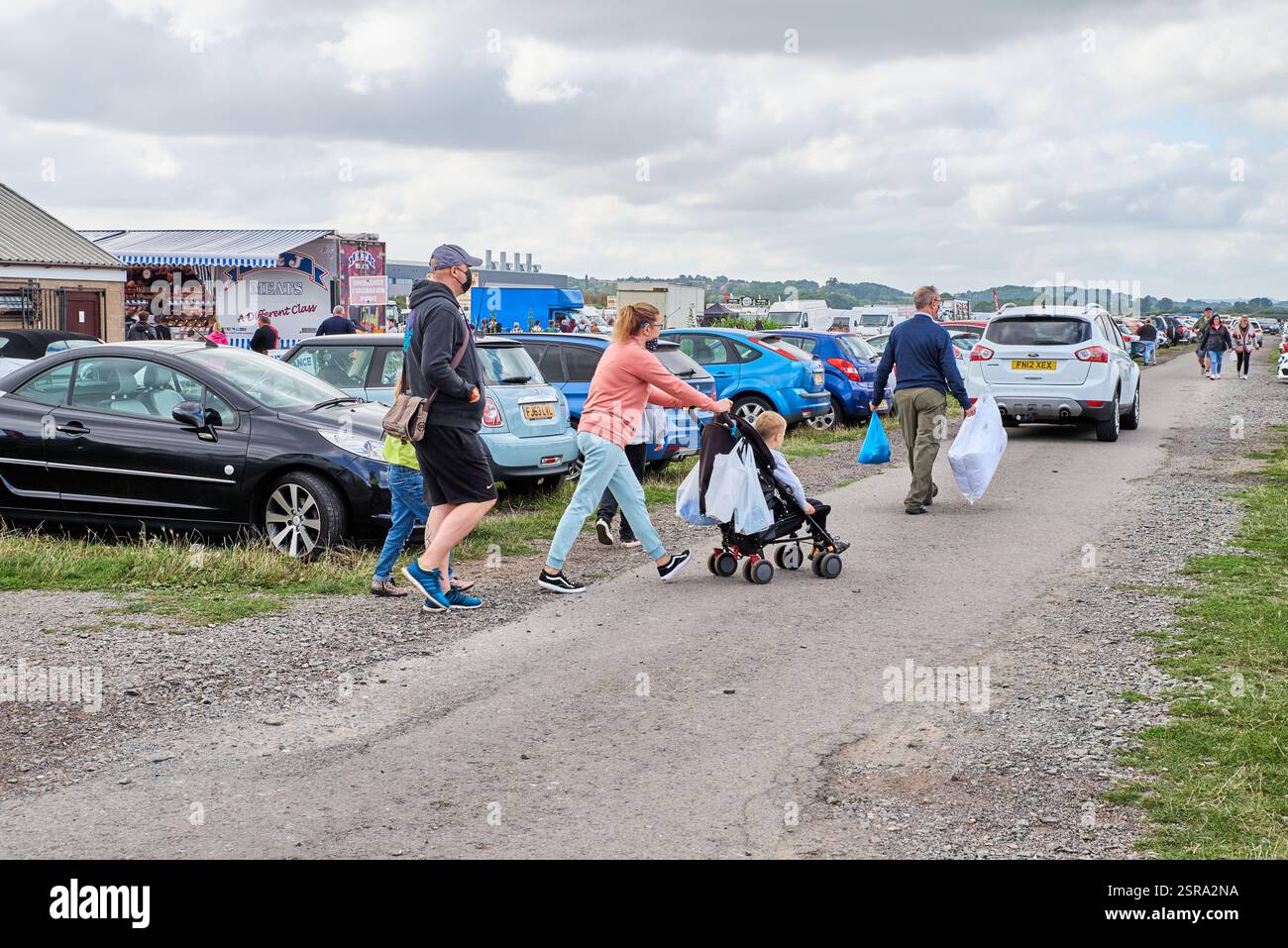 Une jeune famille avec un buggy et des sacs de shopping retournant au parking du Wellesbourne Airfield Market, qui a eu lieu les week-ends et jours fériés. Banque D'Images