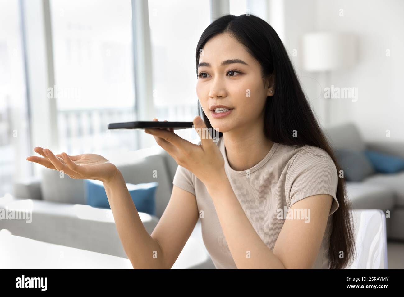 Femme asiatique tenant un smartphone enregistrant des messages vocaux, ayant une conversation téléphonique à haut-parleur Banque D'Images