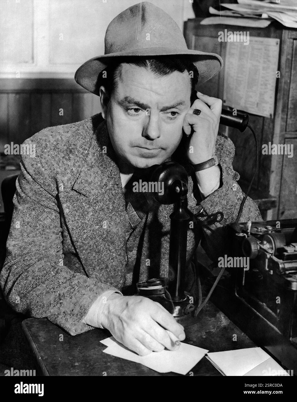 Homme et affaires costume et chapeau assis devant une machine à écrire parlant sur un téléphone à l'ancienne avec votre paix jusqu'à son oreille Banque D'Images