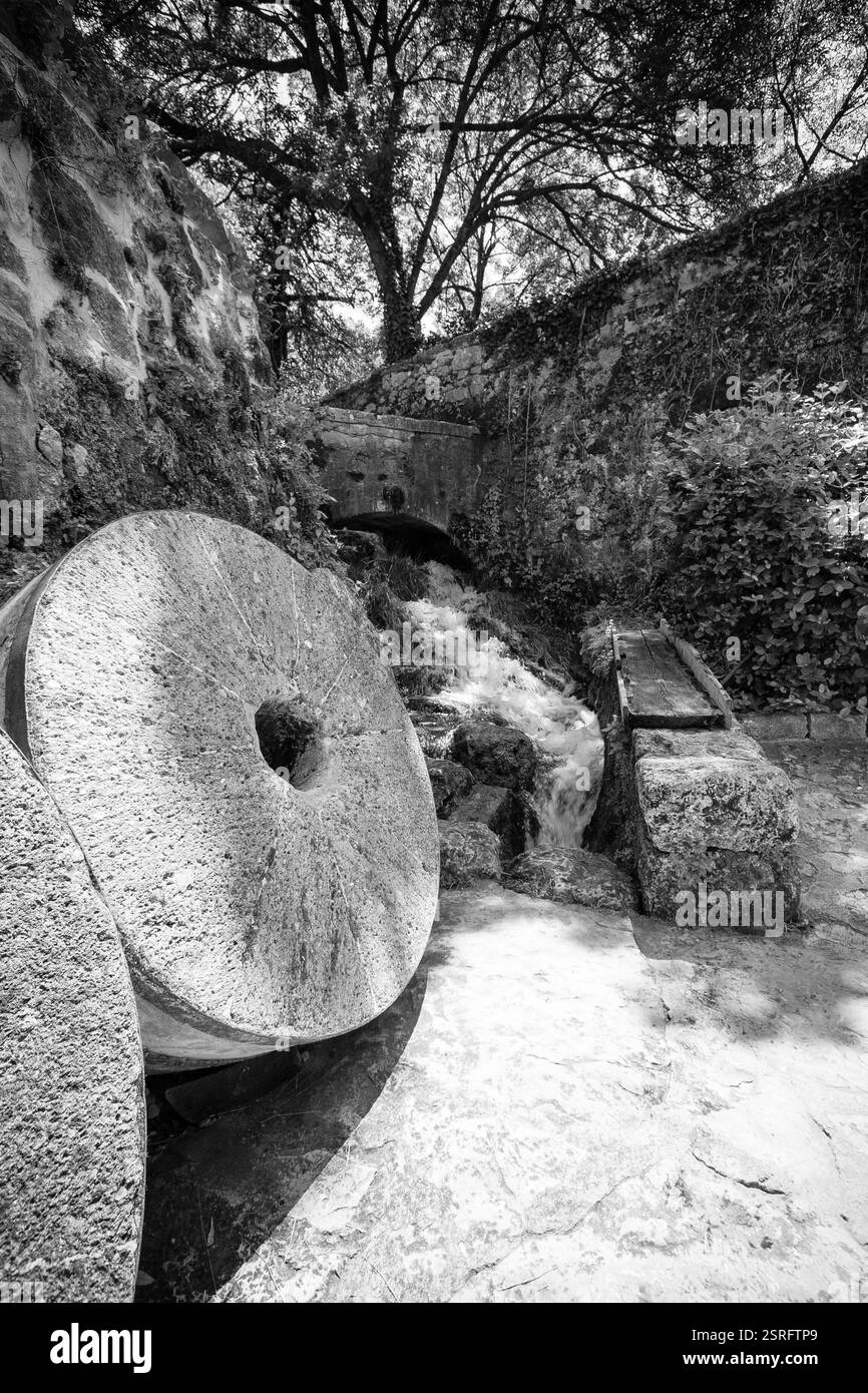Un vieux moulin à eau en pierre dans le parc national de Krka, Croatie, avec des meules reposant à côté d'un ruisseau précipité, capturé en noir et blanc. Banque D'Images