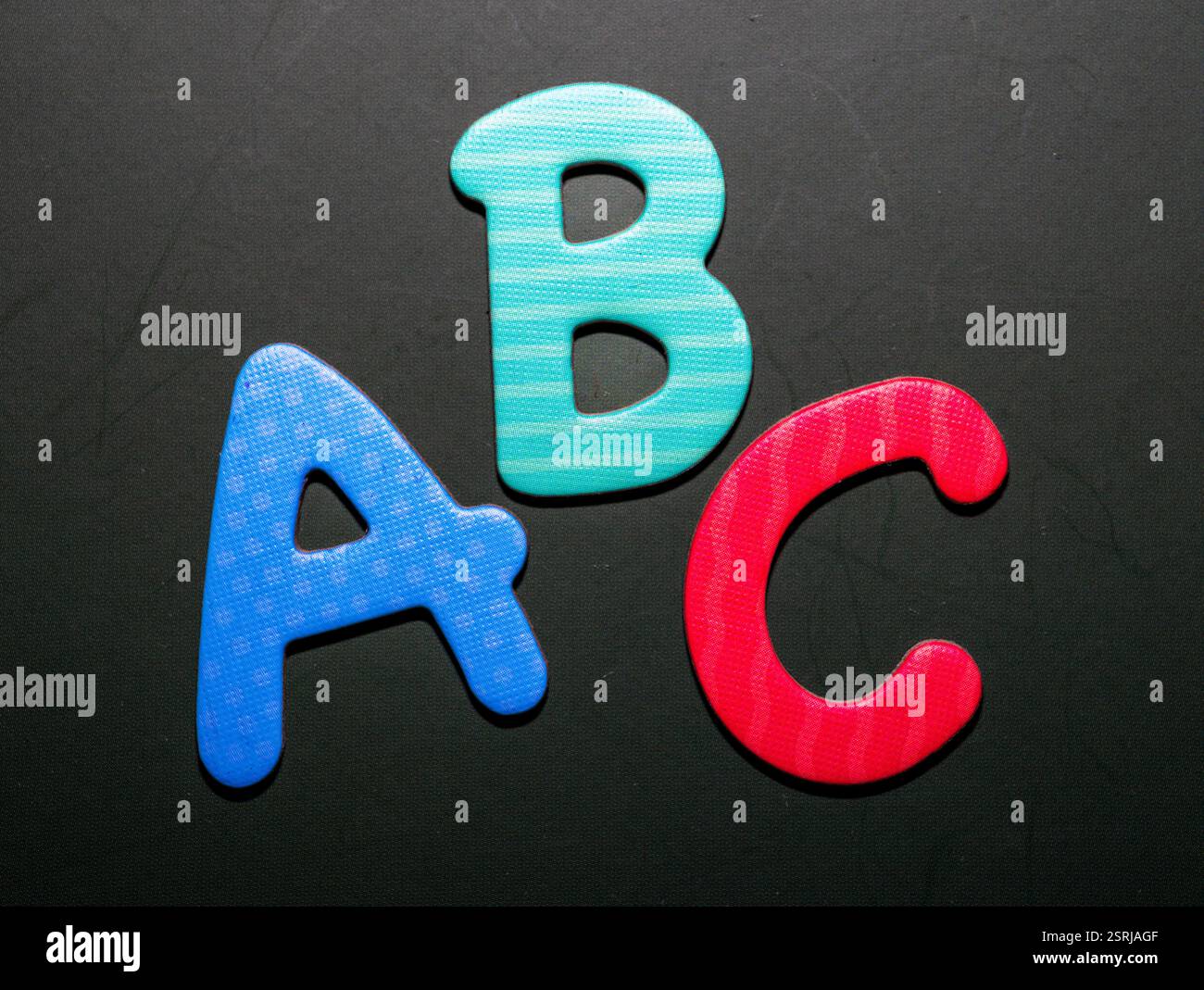 Trois lettres colorées en mousse — “a”, “b” et “c” — disposées sur un fond sombre, symbolisant l’éducation de la petite enfance, l’apprentissage de l’alphabet Banque D'Images