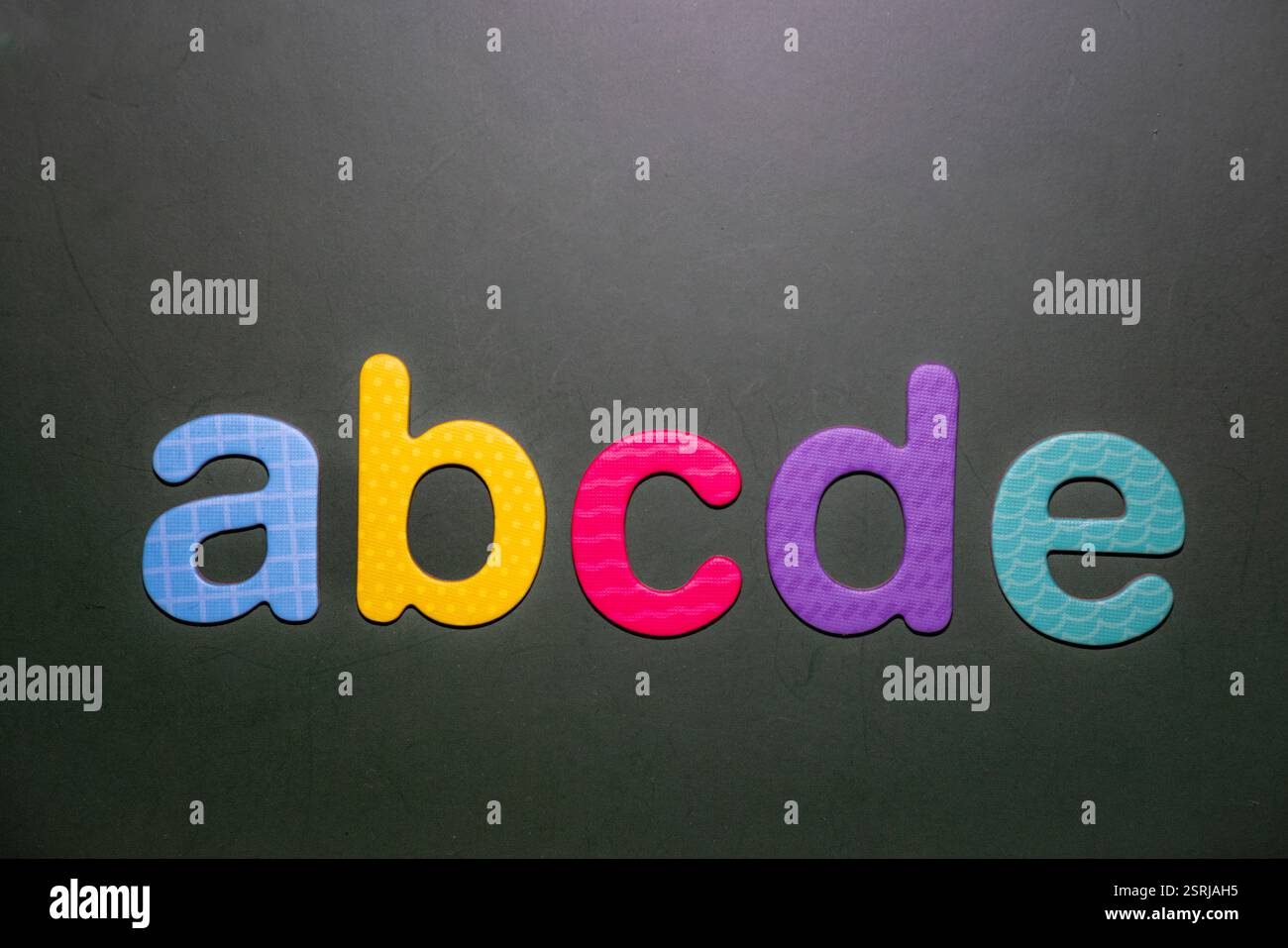 Lettres en mousse colorées a, b, c, d, e disposées sur un fond sombre, symbolisant l'apprentissage précoce, l'alphabétisation et le design créatif. Banque D'Images