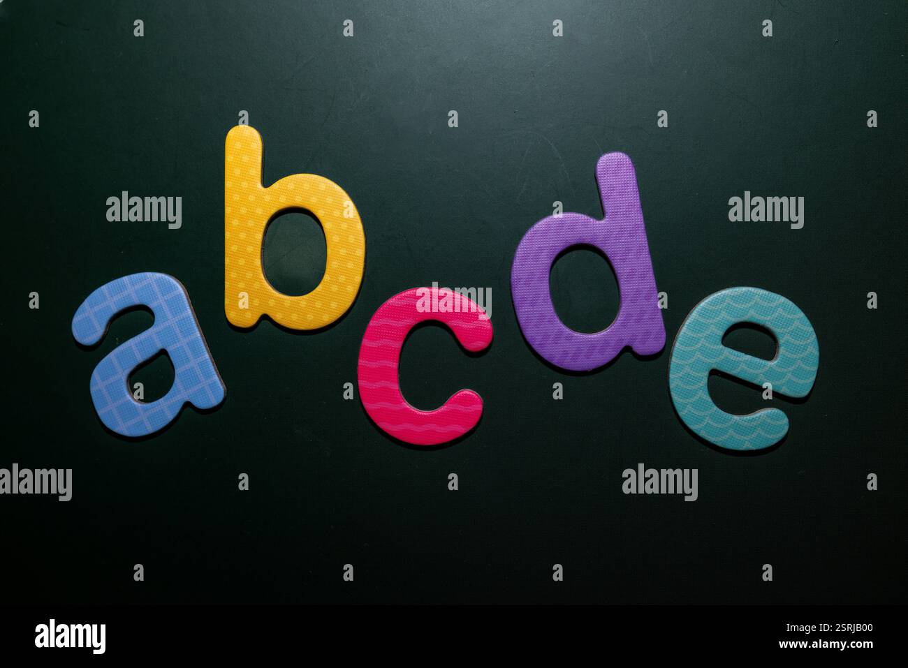 Lettres en mousse colorées a, b, c, d, e disposées sur un fond sombre, symbolisant l'apprentissage précoce, l'alphabétisation et le design créatif. Banque D'Images