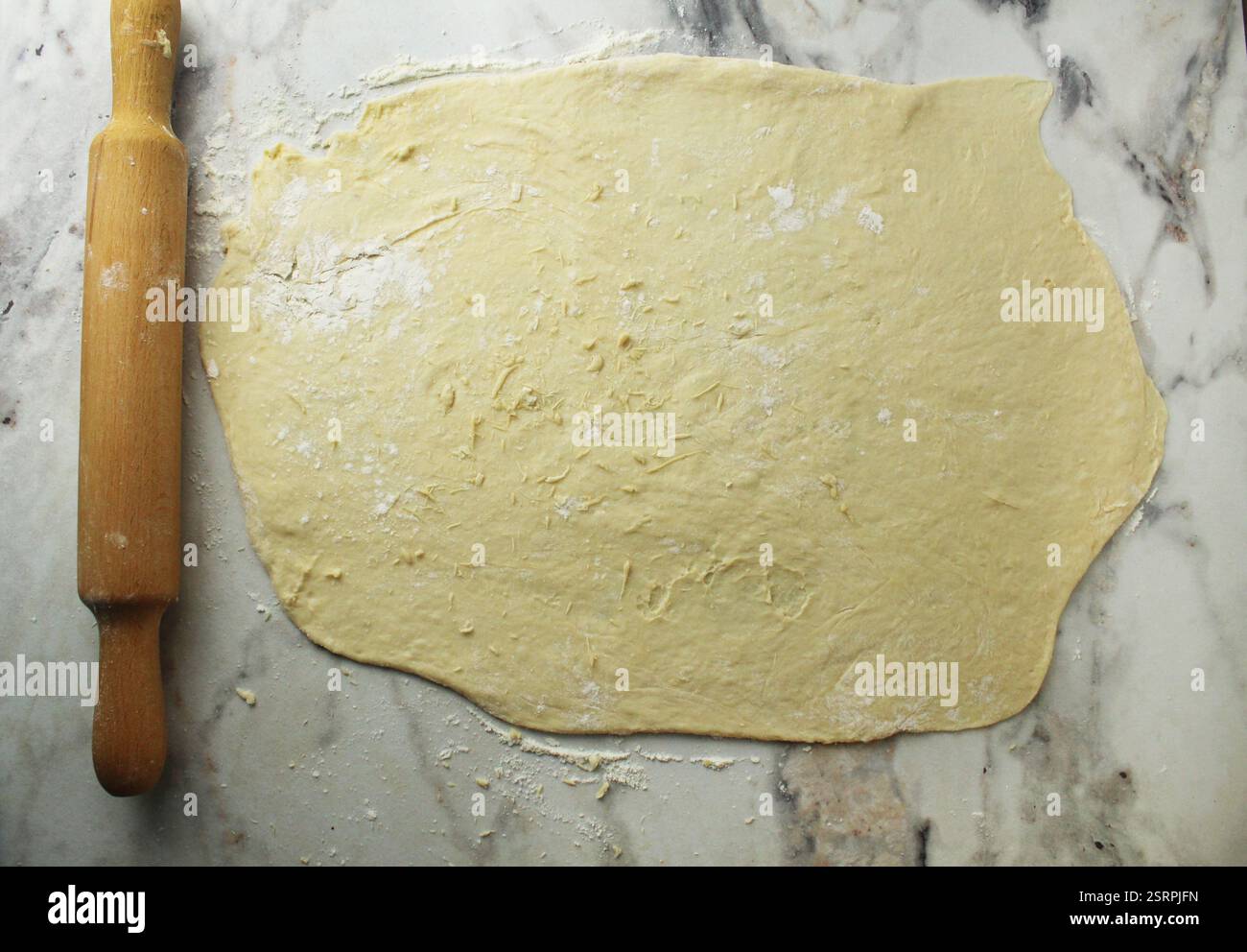 Rouler une couche de pâte levante sur une table avec de la farine. Banque D'Images