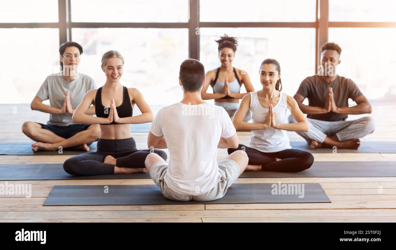 Groupe de personnes pacifiques pratiquant le yoga avec entraîneur dans le studio de gym Banque D'Images