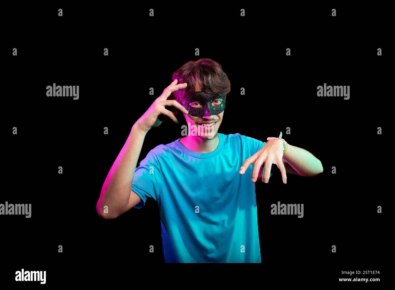 Heureux beau jeune homme portant un masque de carnaval regardant et faisant des gestes de la main à la caméra. Isolé sur fond noir. Brésil Banque D'Images