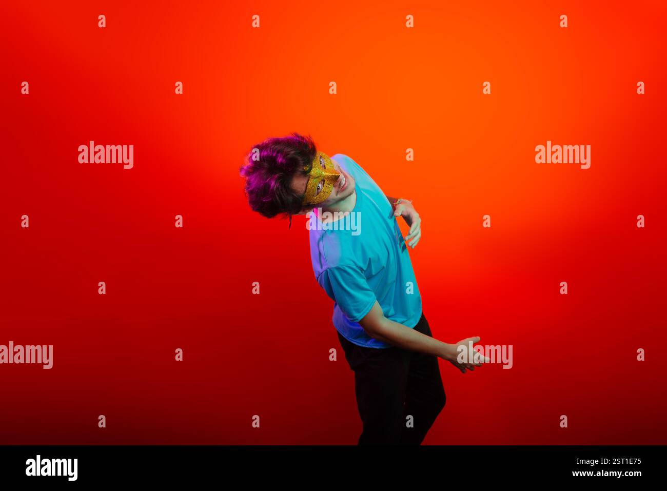 Heureux beau jeune homme portant un masque de carnaval regardant et faisant des gestes de la main à la caméra. Isolé sur fond de néon orange. Brésil Banque D'Images