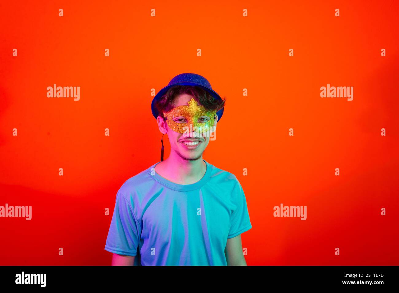 Beau jeune homme portant un masque de carnaval et regardant la caméra. Heureux et amusant. Isolé sur fond de néon orange. Brésil Banque D'Images
