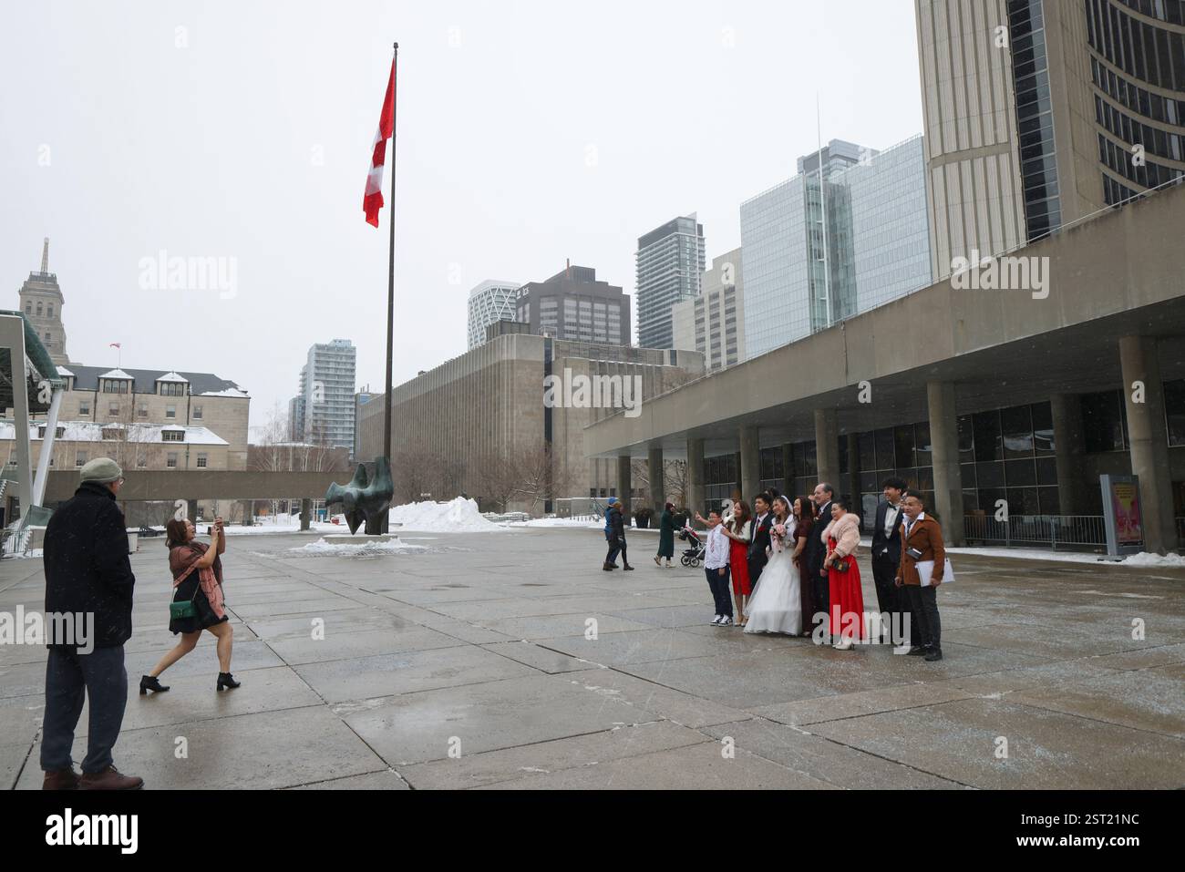 Toronto, Canada.15 février 2025. Les jeunes mariés et leurs amis posent pour une photo de groupe à côté d'un drapeau canadien géant devant l'hôtel de ville de Toronto le 15 février 2025 à Toronto, Canada. Un drapeau canadien géant mesurant 30 pieds de long et 15 pieds de large a été hissé devant l'hôtel de ville le 15 février pour marquer le 60e anniversaire de l'inauguration du drapeau canadien. Crédit : Yu Ruidong/China News Service/Alamy Live News Banque D'Images