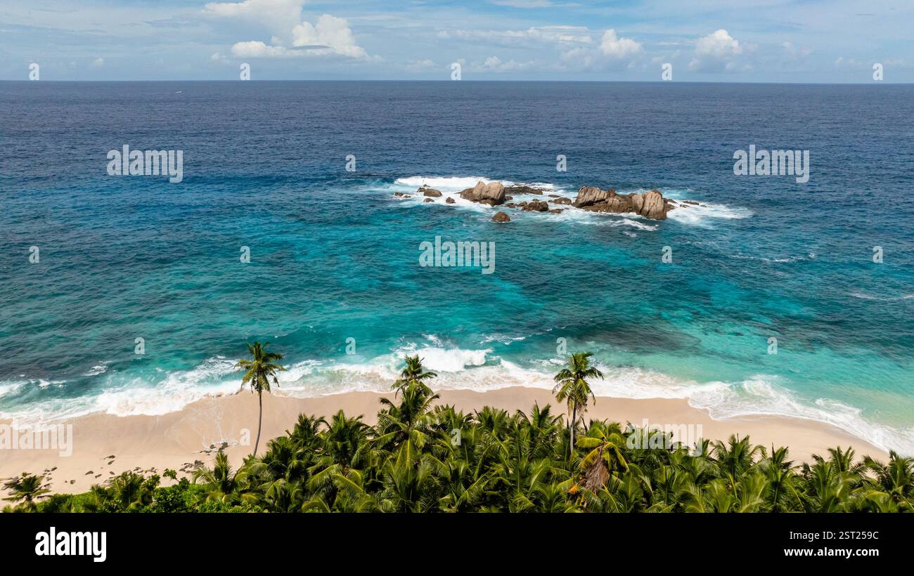 Rochers dispersés dans l'eau turquoise près de la plage avec des vagues se brisant sur le rivage. Anse Boileau. Seychelles, Mahé. Banque D'Images