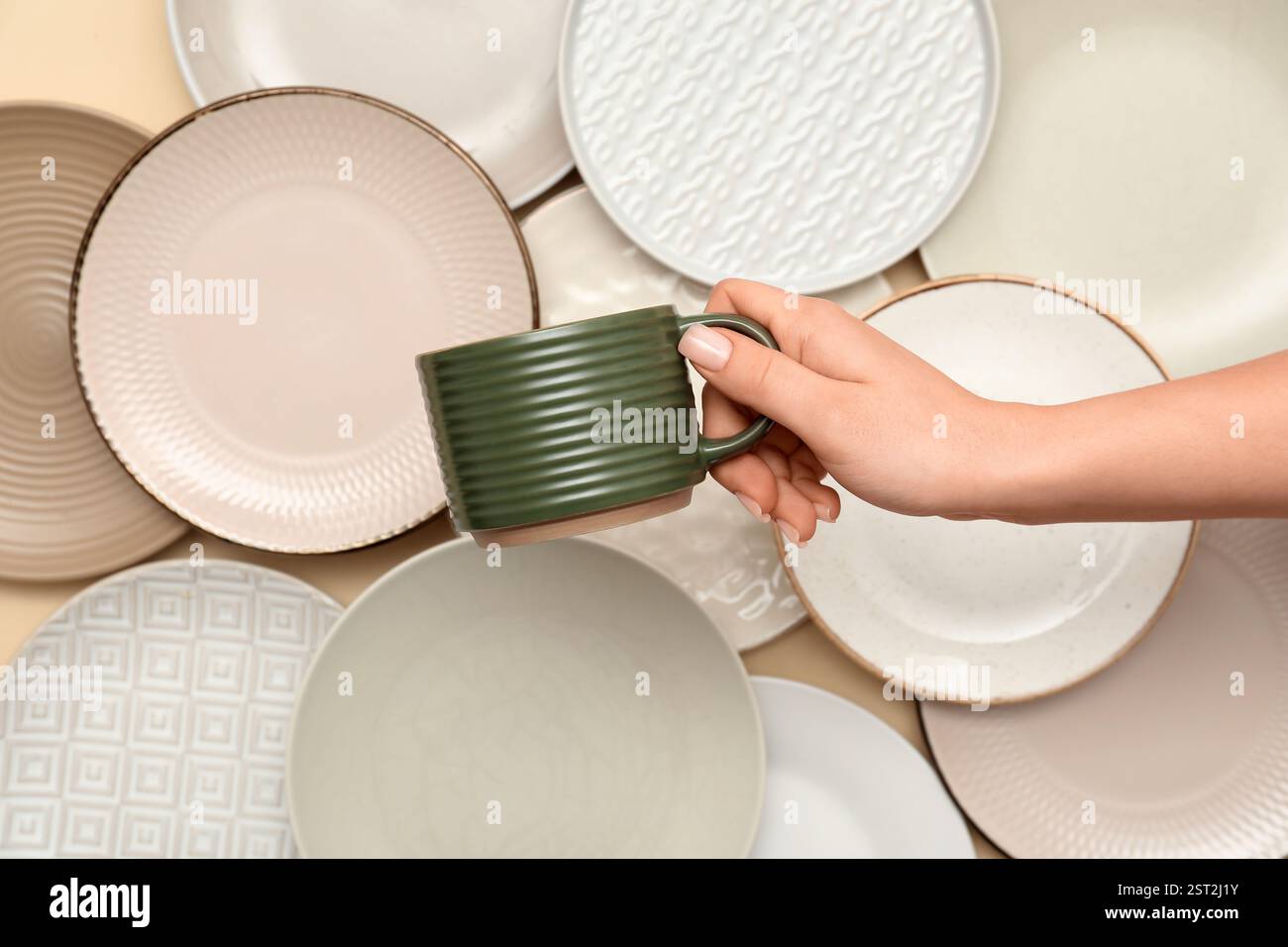Main femelle avec tasse en céramique verte et plaques sur fond beige Banque D'Images