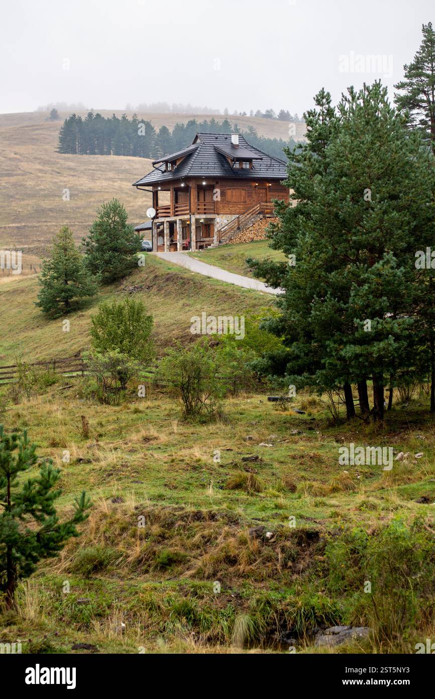 Grande maison moderne en bois et en pierre à la fin de la route sur le sommet de la colline avec des pins Banque D'Images