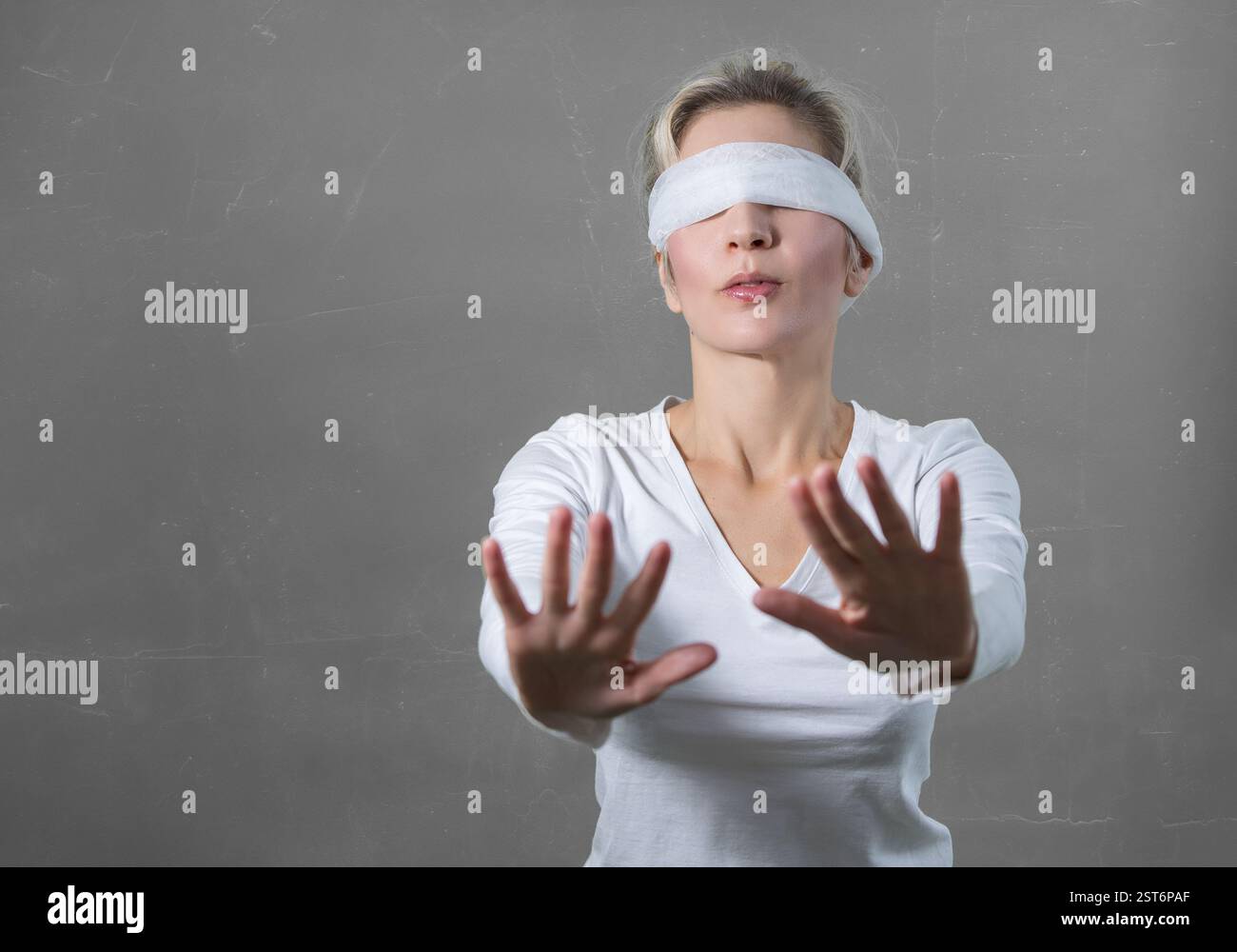 Femme les yeux bandés avec les mains atteignant vers l'avant et grope dans l'obscurité sur un fond de mur gris Banque D'Images