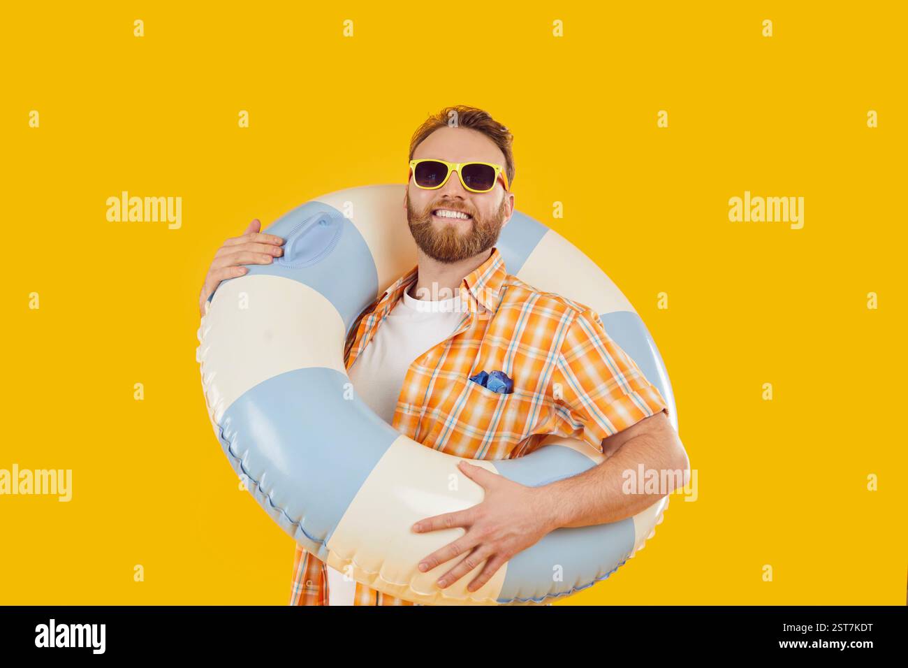 Portrait d'homme joyeux tenant une grande bouée de sauvetage gonflable bleue et blanche sur fond jaune. Banque D'Images