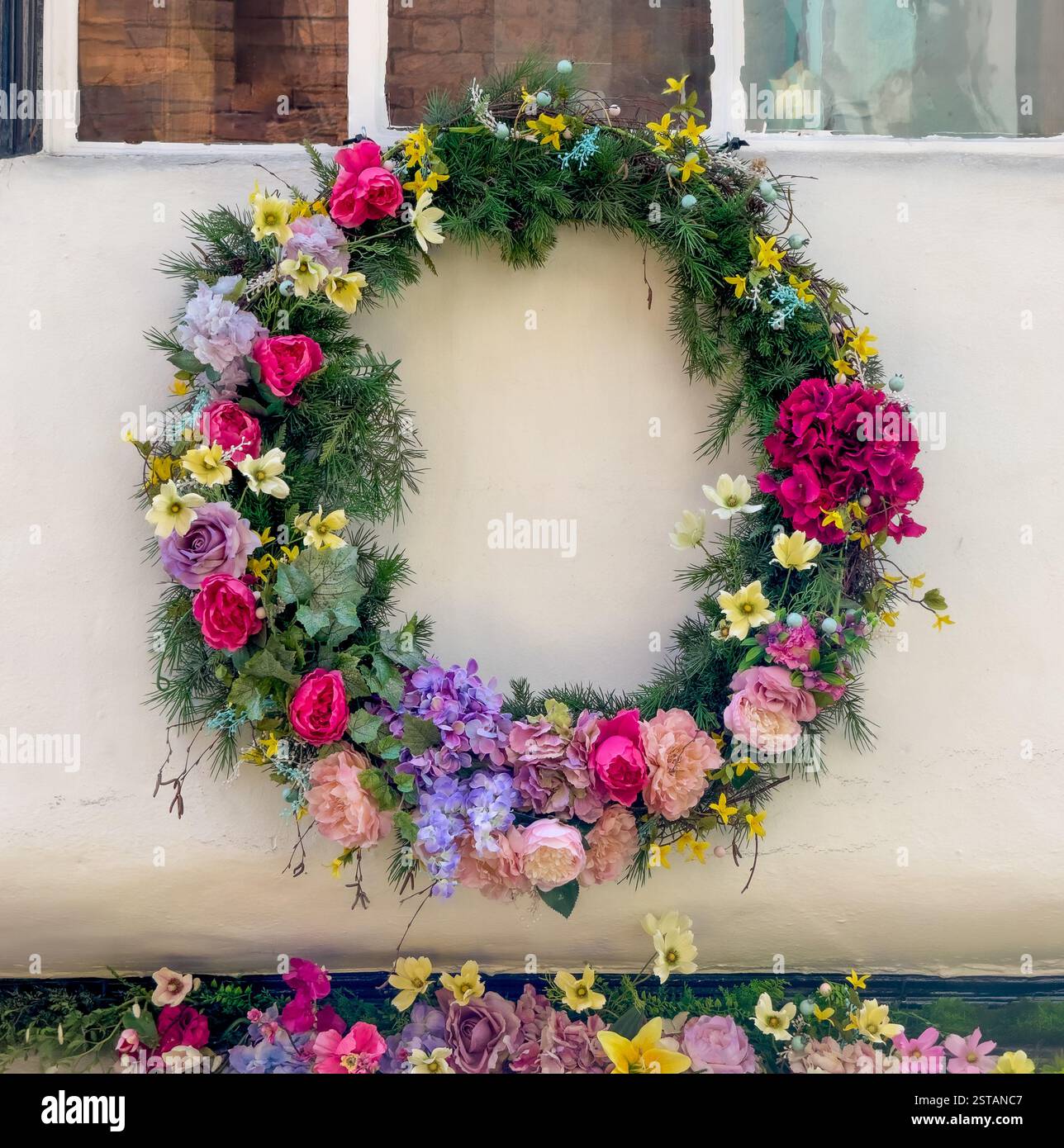 Couronne d'été confectionnée à partir de fleurs de soie dans des teintes roses, mauves et jaunes ornant le mur extérieur blanc d'une maison. ROYAUME-UNI Banque D'Images
