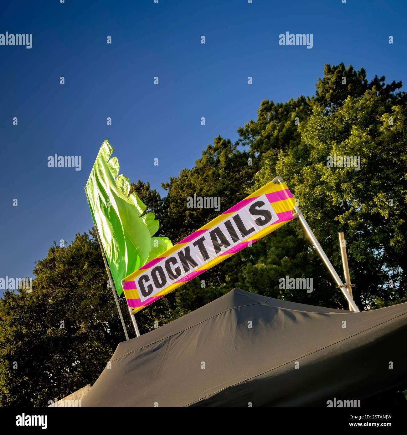 Plan incliné d'un panneau de stand de cocktail et drapeau vert vif du festival contre un ciel bleu clair Banque D'Images