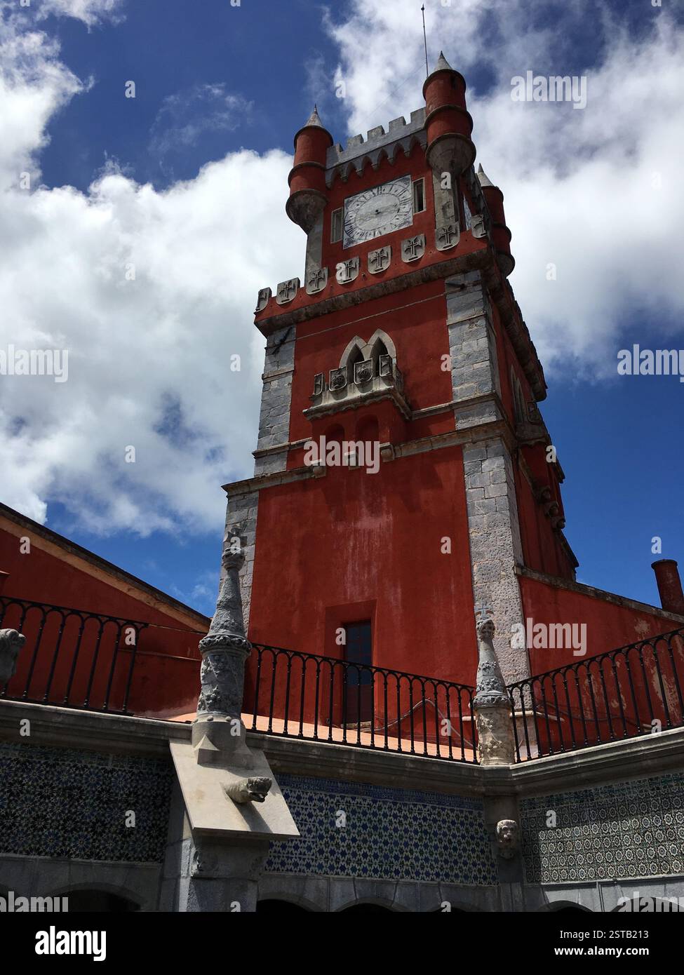 Le palais de Pena, une structure rouge éclatante aux détails complexes, se dresse haut contre un ciel bleu clair. Une tour majestueuse ornée d'une horloge et de flèches Banque D'Images