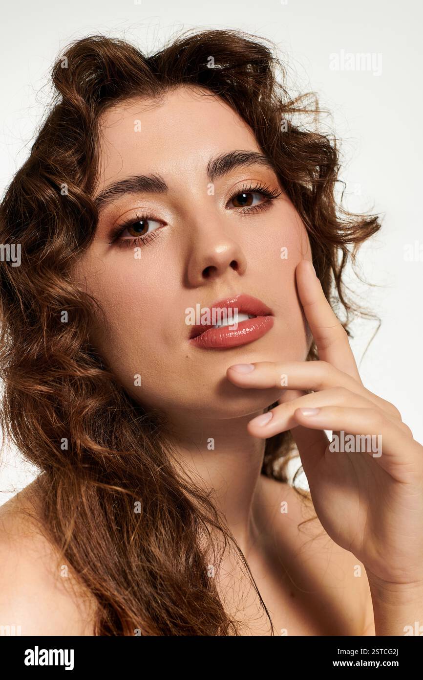 Une jeune femme captivante aux cheveux bouclés pose gracieusement dans une lumière vive. Banque D'Images