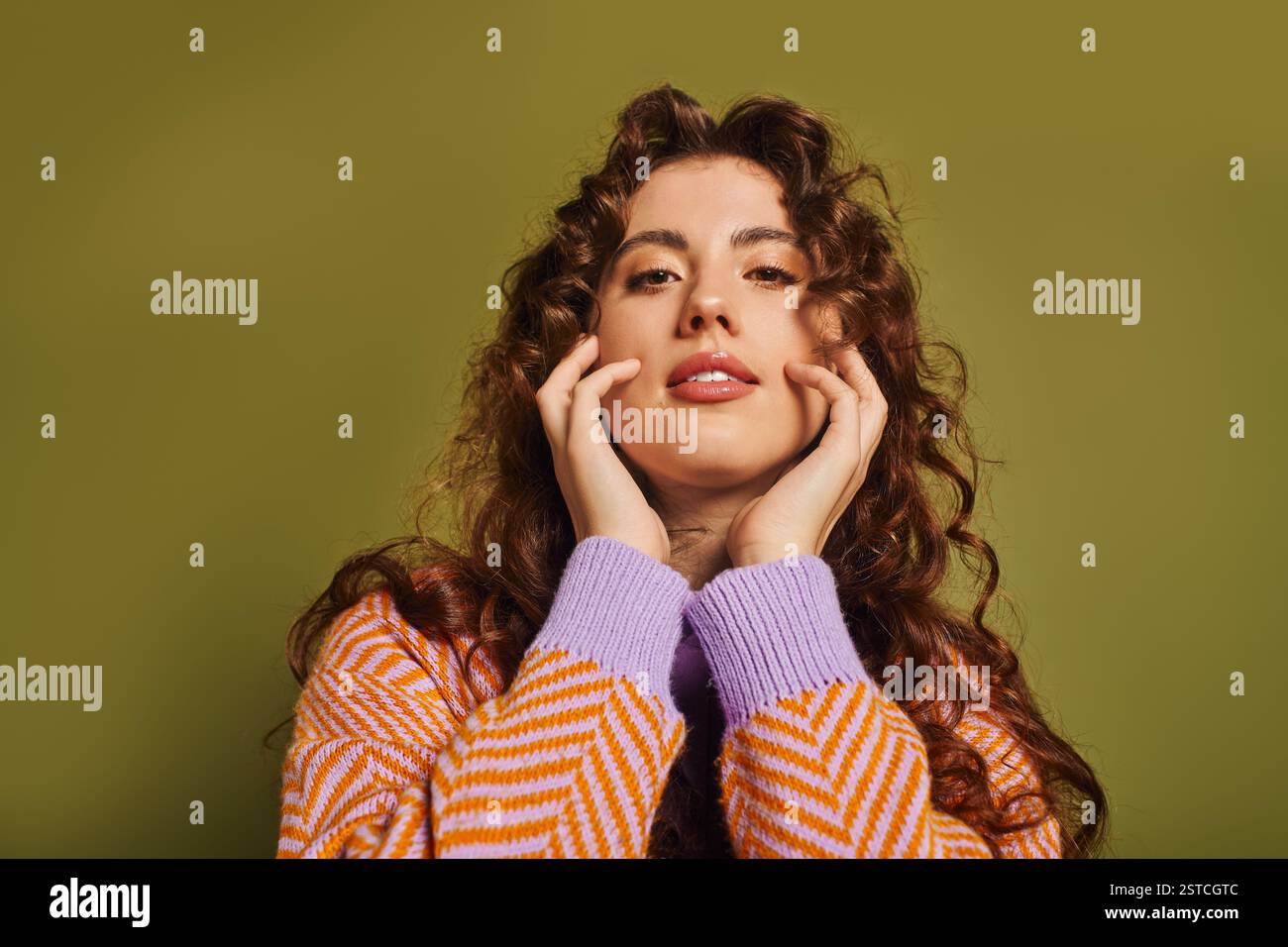 Jeune femme aux cheveux bouclés pose en toute confiance, soulignant sa tenue élégante et son charme radieux. Banque D'Images