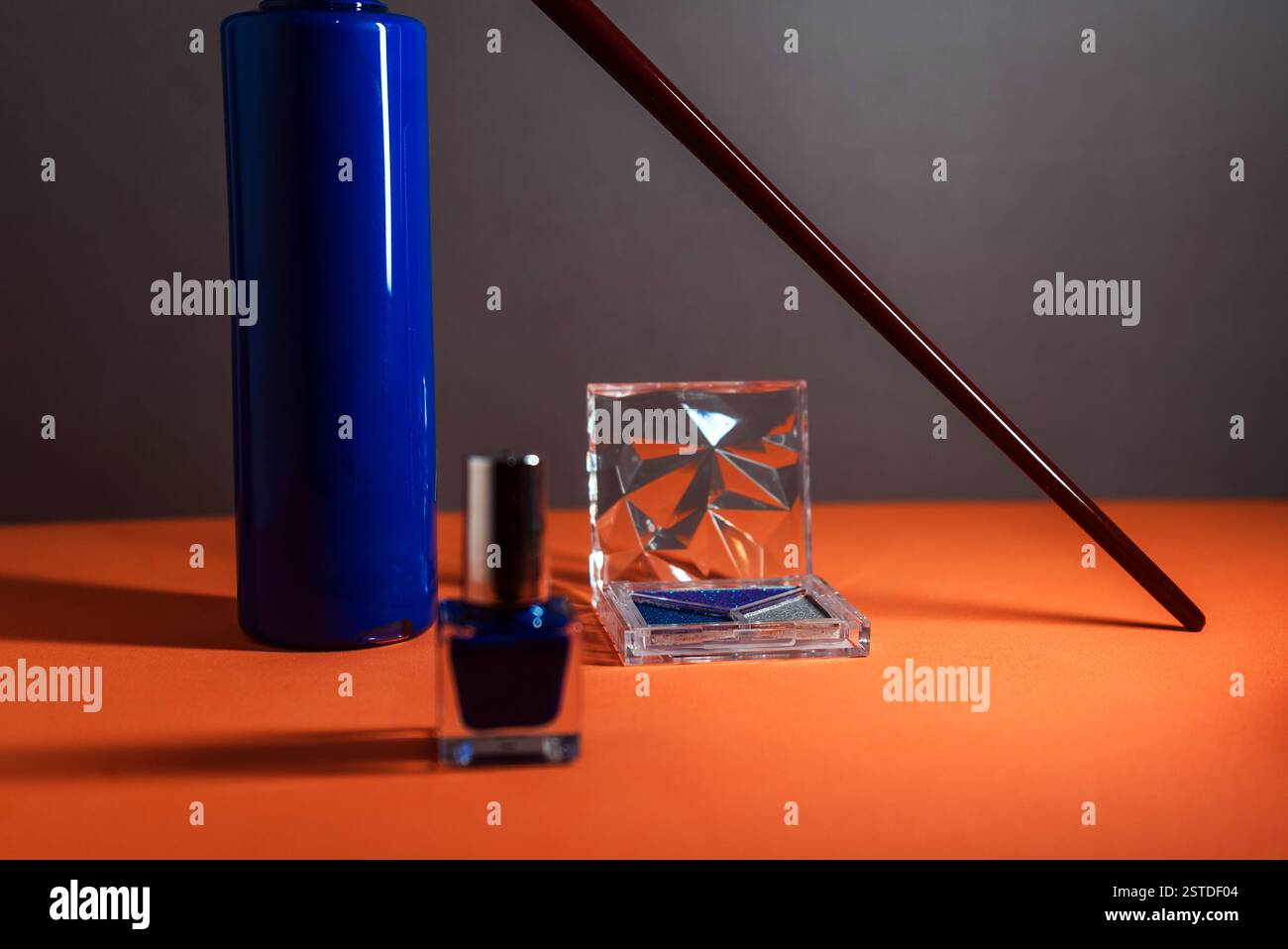 vernis à ongles bleu vif et articles de maquillage dans un arrangement artistique sur un fond orange. Banque D'Images
