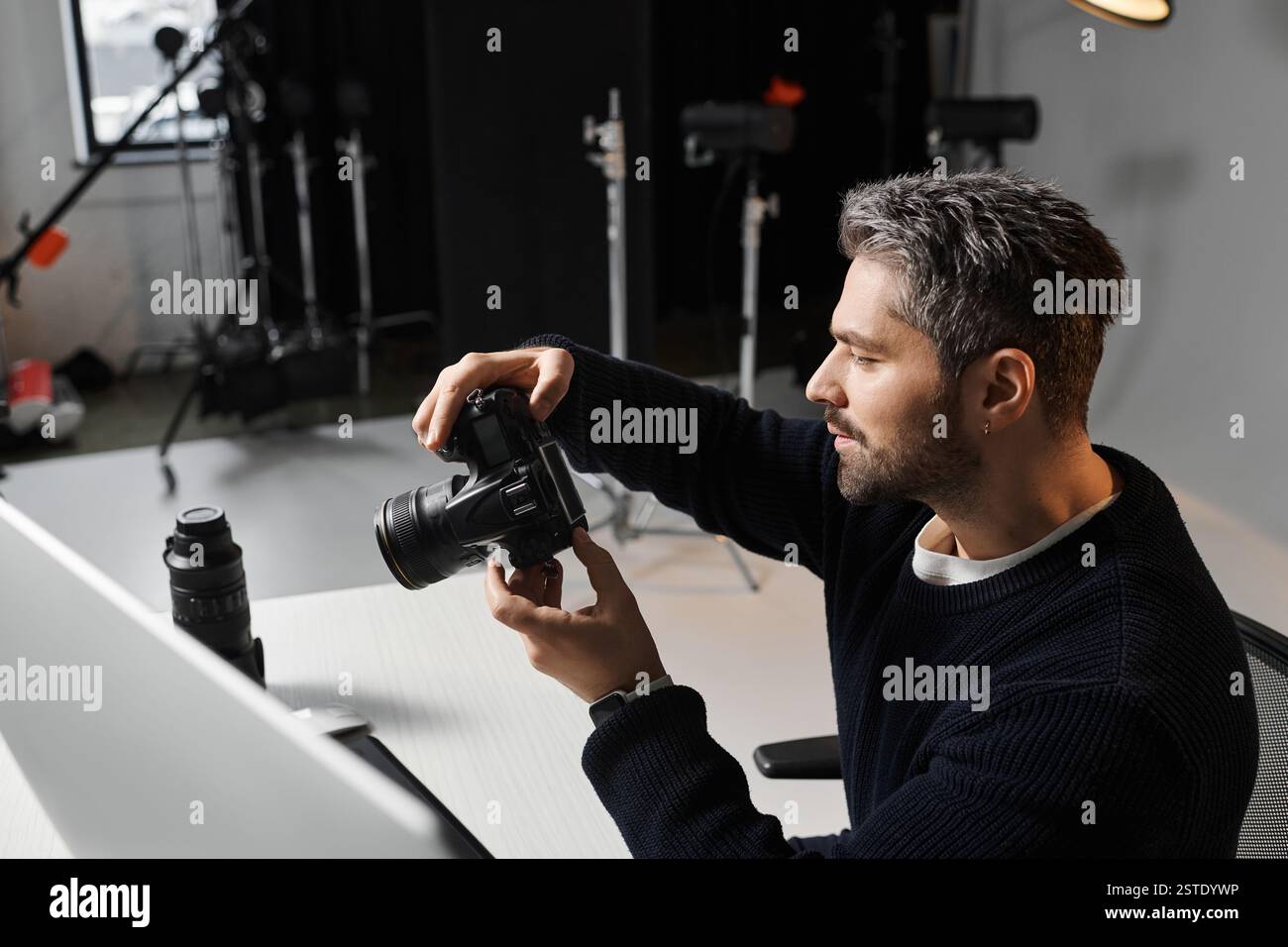 Un homme concentré examine les réglages de sa caméra avant de commencer une séance créative dans un studio moderne. Banque D'Images