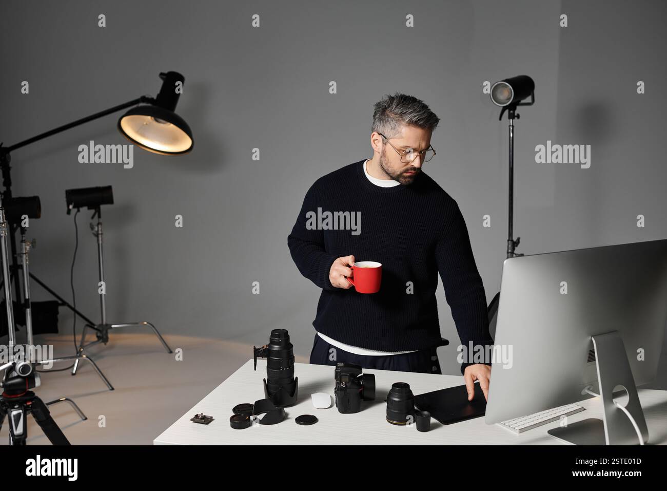 Un homme prend une boisson chaude tout en préparant son équipement dans un studio de photographie élégant. Banque D'Images
