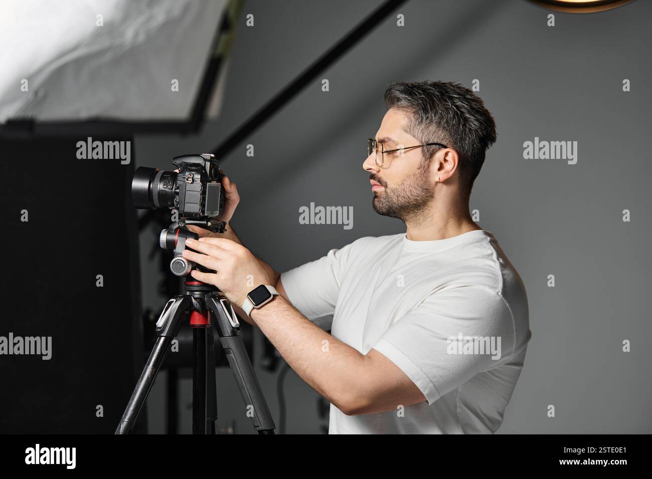 Un photographe qualifié se concentre sur le perfectionnement des réglages de l'appareil photo dans un studio contemporain. Banque D'Images