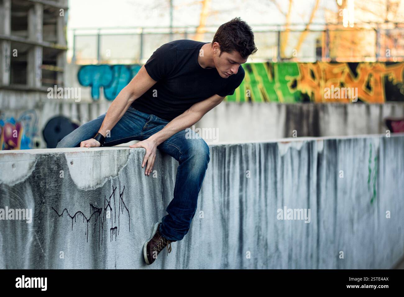 Jeune homme assis et en équilibre sur un mur sale Banque D'Images