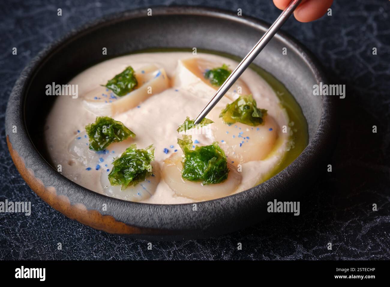 D'en haut de la culture personne anonyme mangeant une délicieuse soupe de crème cuite avec des herbes et des noix de Saint-Jacques servi dans un bol placé sur la table Banque D'Images