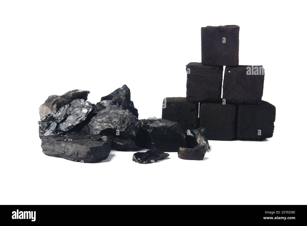 Une collection de briquettes de charbon naturel et de charbon de bois soigneusement empilées, prises sur un fond blanc Uni qui souligne leur texture et leur couleur. Banque D'Images