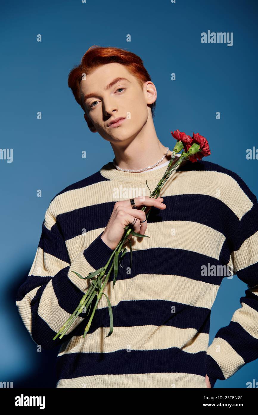 Un homme jeune et beau tient des fleurs rouges, mettant en valeur une expression réfléchie et émotionnelle. Banque D'Images