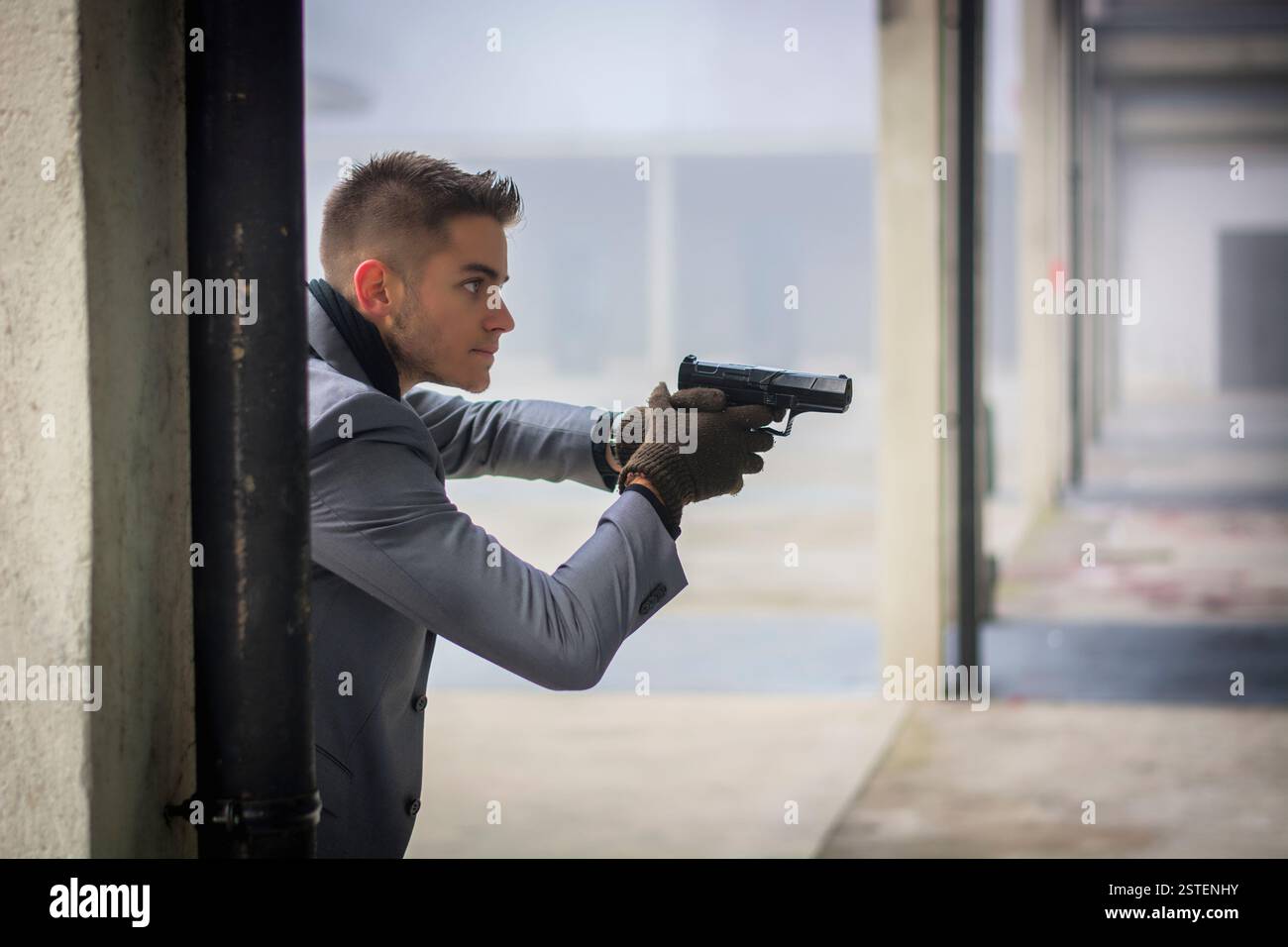 Bien habillé beau jeune détective ou policier ou gangster debout dans un environnement urbain tenant un pistolet avec un déterminé e Banque D'Images