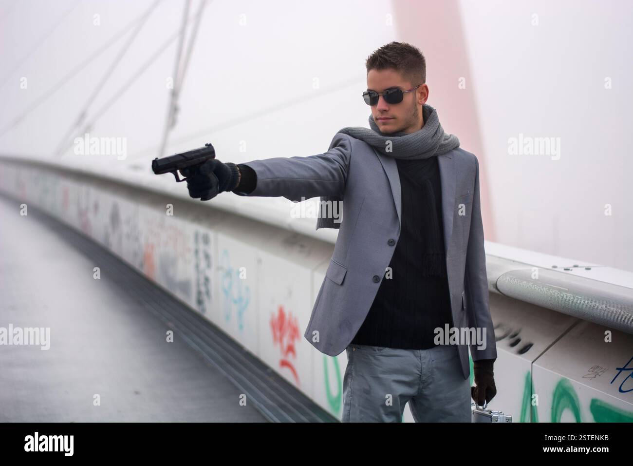 Bien habillé beau jeune détective ou policier ou gangster debout dans un environnement urbain visant une arme au côté gauche Banque D'Images