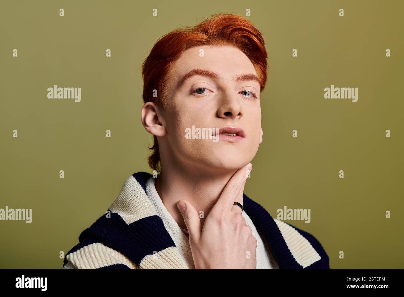 Jeune homme émotionnel avec les cheveux roux pose soigneusement d'une manière détendue et élégante, embrassant le charme. Banque D'Images