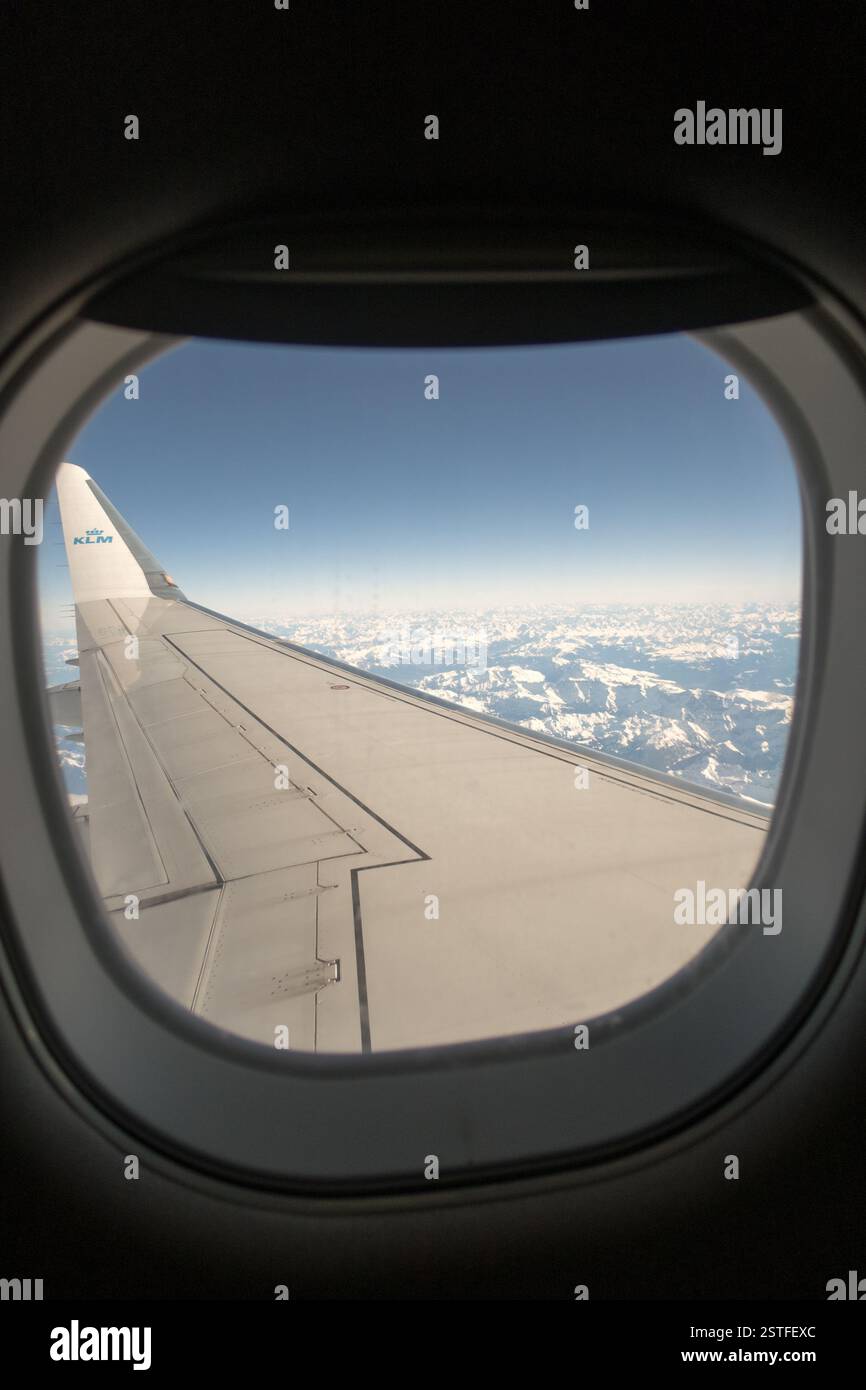 Une vue imprenable depuis la fenêtre passager d'un avion KLM, survolant des montagnes enneigées avec l'emblématique bout des ailes en vue. Banque D'Images