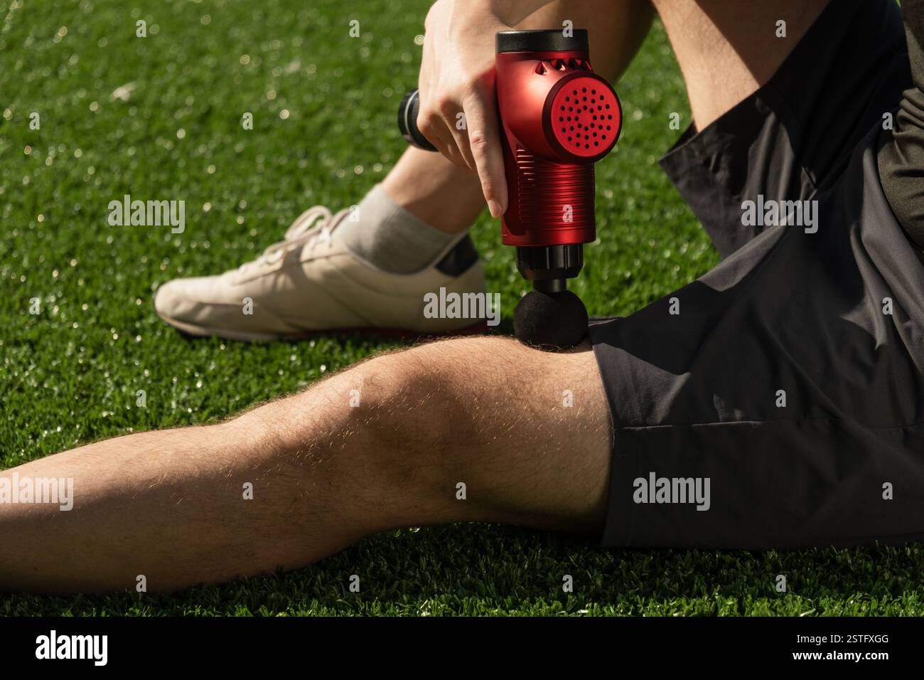 Homme massant les jambes avec le pistolet à percussion de massage après l'entraînement. Pistolet masseur à percussion thérapeutique. Banque D'Images