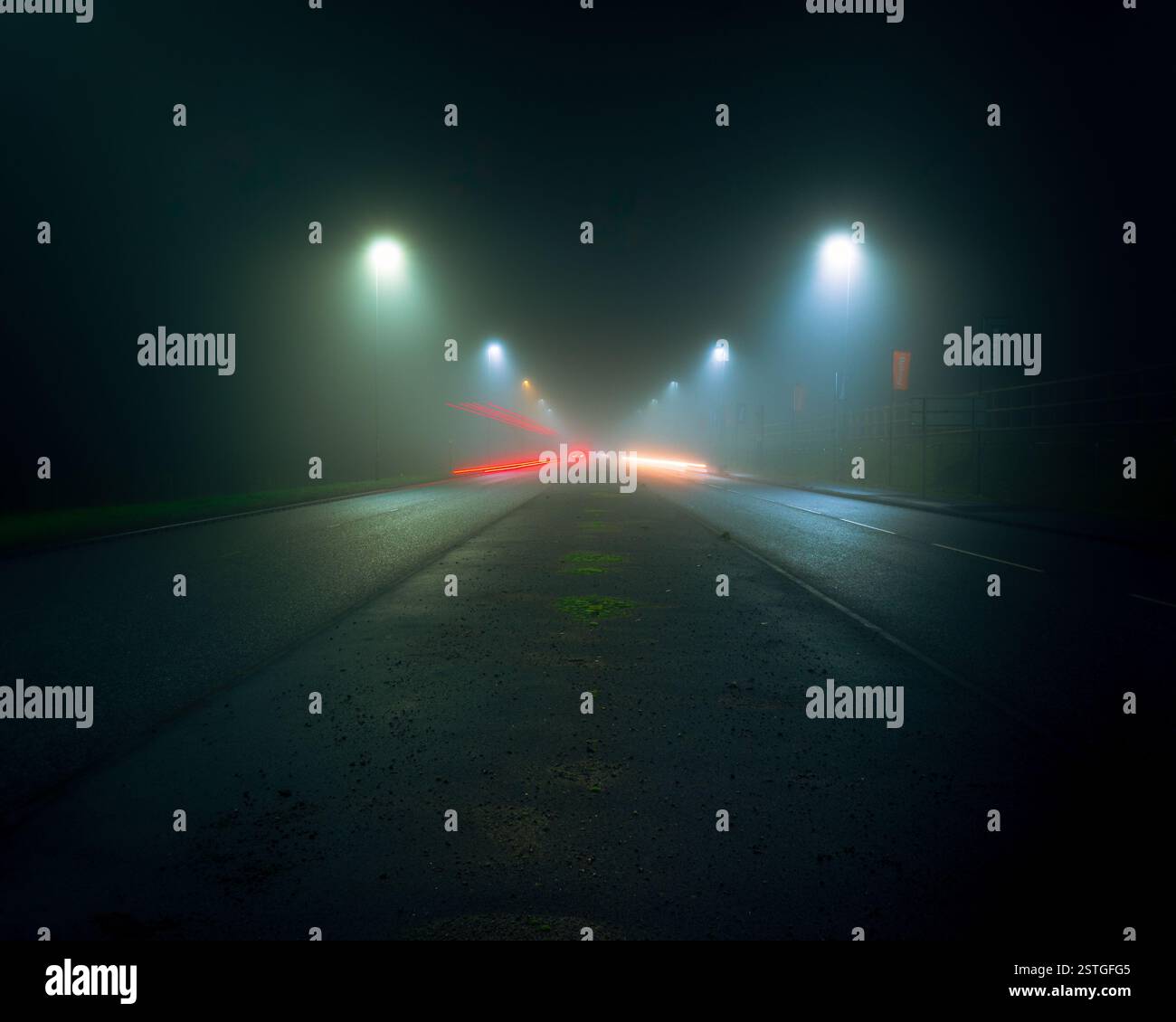 Une photo longue exposition de voitures circulant le long d'une route vide dans une zone industrielle par une nuit brumeuse Banque D'Images