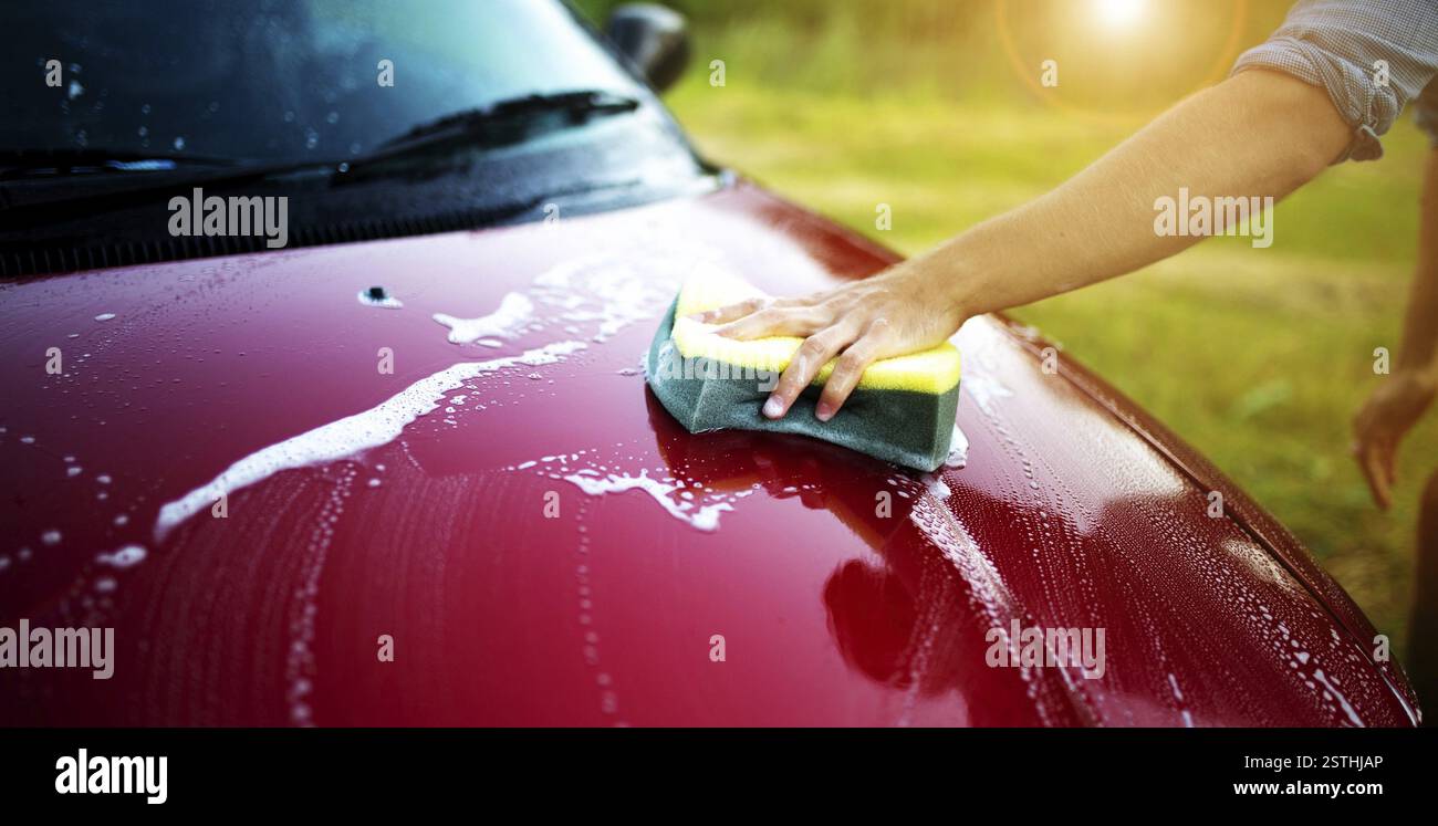 Nettoyage à la main d'une voiture rouge avec une éponge sous la lumière du soleil Banque D'Images Nettoyage à la main d'une voiture rouge avec une éponge sous la lumière du soleil Banque D'Images