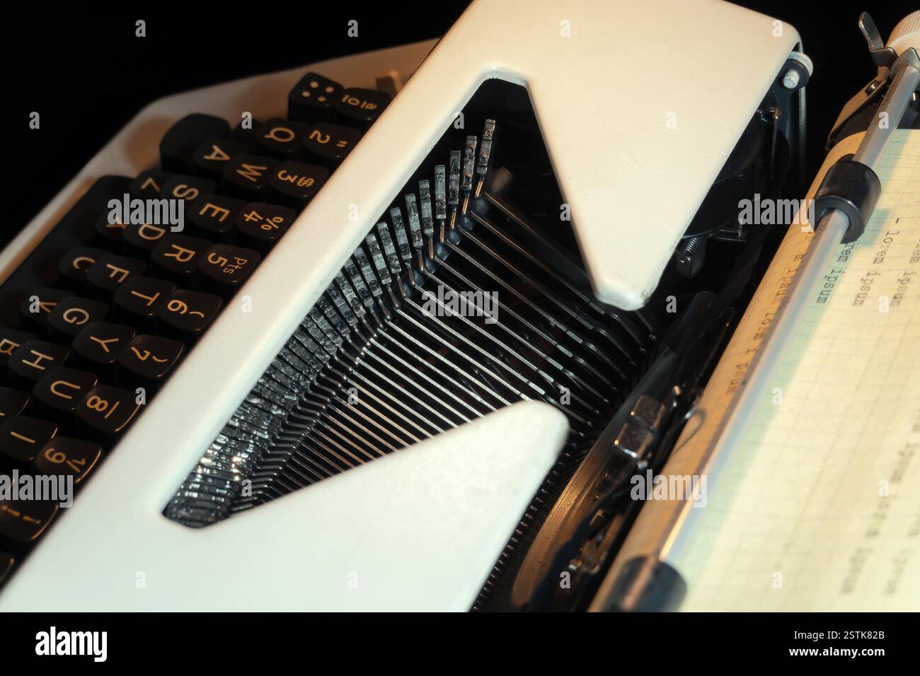Gros plan détaillé d'une machine à écrire ancienne avec des touches noires et des barres à caractères métalliques, avec un rouleau de papier chargé sur la platine. Idéal pour les thèmes de w Banque D'Images