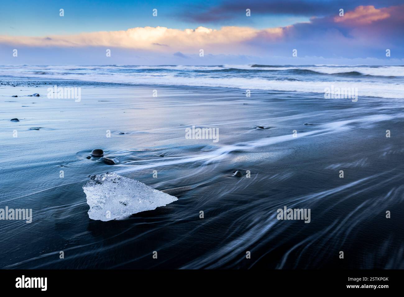 Vue sur les vagues de la mer qui coulent autour des blocs de glace au coucher du soleil sur la célèbre plage Diamond. Jökulsárlón, Diamond Beach, Austurland, Islande, Europe du Nord. Banque D'Images