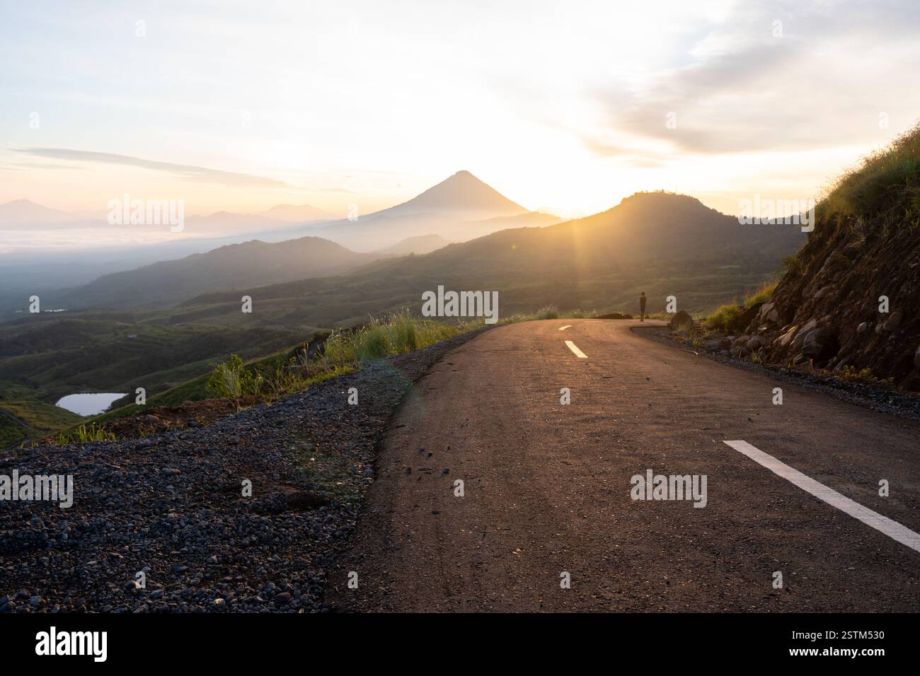Un lever de soleil à couper le souffle sur une route de montagne sinueuse, entourée de vallées brumeuses et d'un ciel doré. Parfait pour les voyages, l'aventure et les thèmes de la nature. Banque D'Images